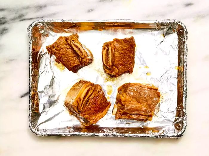 A baking sheet lined with foil, featuring four boiled beef ribs topped with garlic sauce