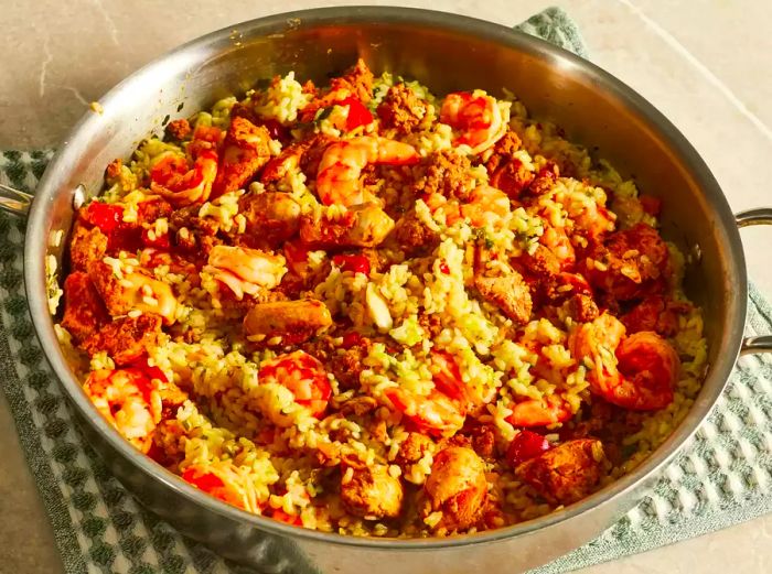 A close-up shot from a mid-angle of a vibrant paella featuring chicken, chorizo, and shrimp in a large skillet, ready to be served.