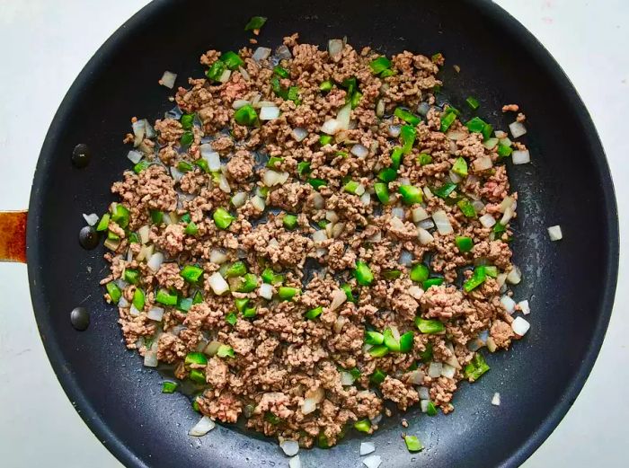 Overhead image showing meat, green peppers, and onions cooking together in a pan