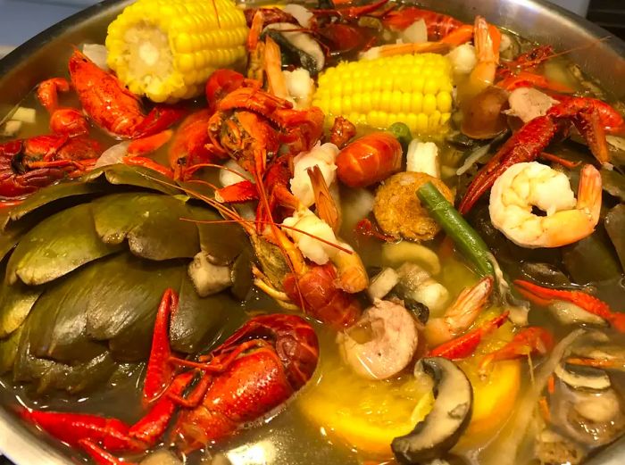 Close-up shot of a Louisiana Crawfish Boil, featuring crawfish, shrimp, corn, mushrooms, oranges, and artichokes.