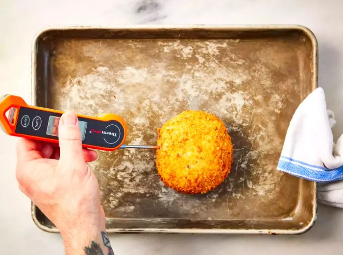 A baking sheet with a perfectly cooked chicken Kiev, with a meat thermometer checking the internal temperature