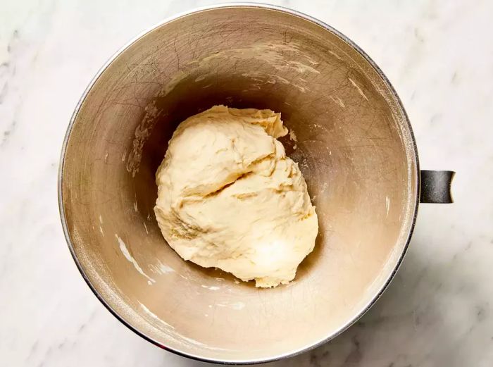 The pizza dough begins to form in the bowl of the stand mixer.