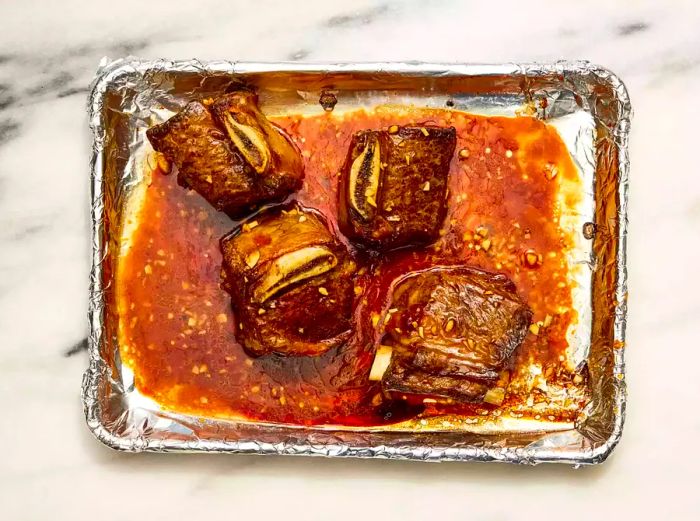 A foil-lined baking sheet with oven-baked short ribs in garlic sauce