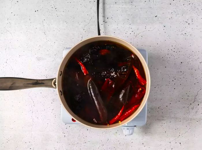 A pot of guajillo, arbol, and ancho chili peppers simmering in water