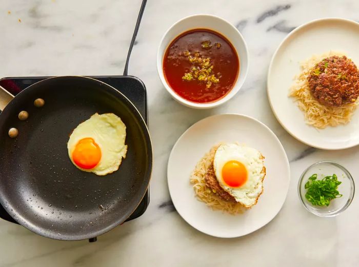 Once the eggs are fried, split the rice between two bowls, add the patties, drizzle with gravy, and top with the fried eggs.