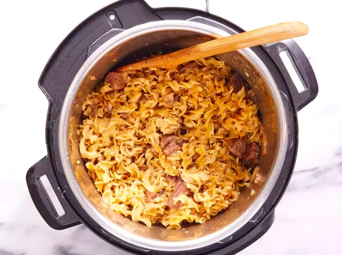 A wooden spoon mixing sour cream into a pot of Beef Stroganoff in the Instant Pot