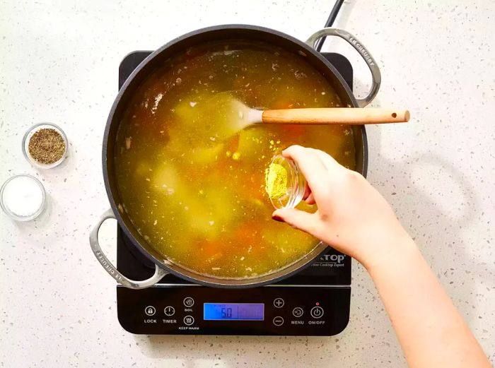 Adding seasonings to homemade chicken soup.