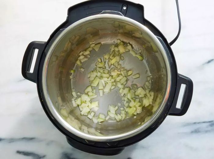 An Instant Pot with chopped onions sautéing in oil