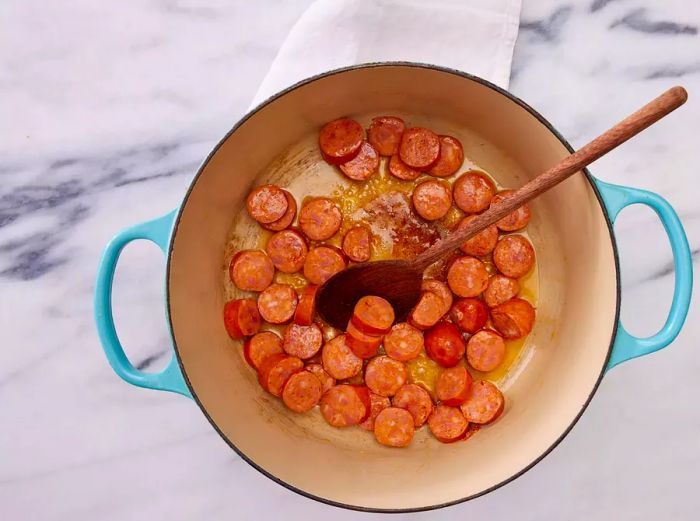 A large pot with butter and sliced sausage cooking together.