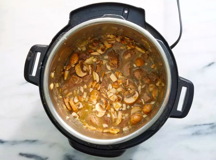 An Instant Pot filled with sliced mushrooms and beef simmering in a rich, thickened chicken broth