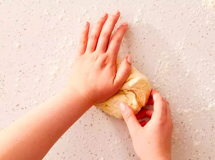 Two hands working the dough on a lightly floured surface