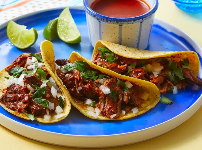 A plate of three birria de res tacos served with sauce on the side