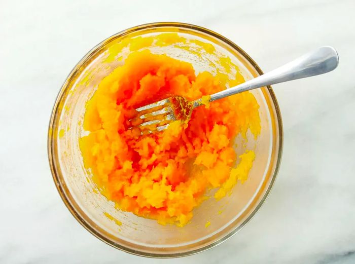 A top view of mashed butternut squash, gently fluffed with a fork in a bowl.