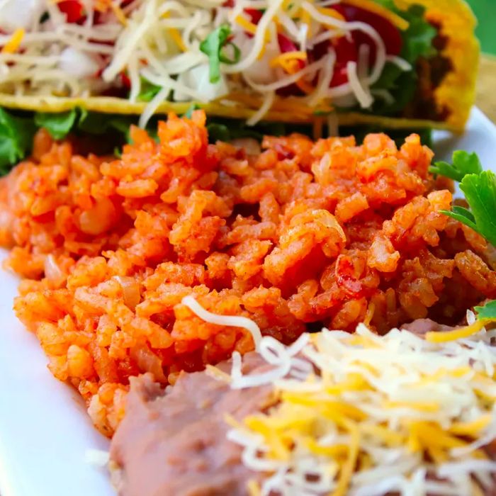 A plate of Mexican rice accompanied by tacos and refried beans, viewed from the side.