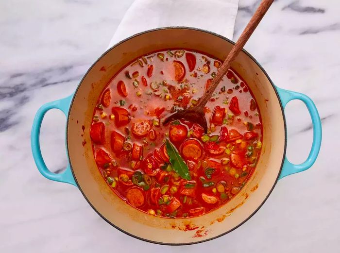 A large pot with chopped vegetables, sausage, rice, and chicken broth.