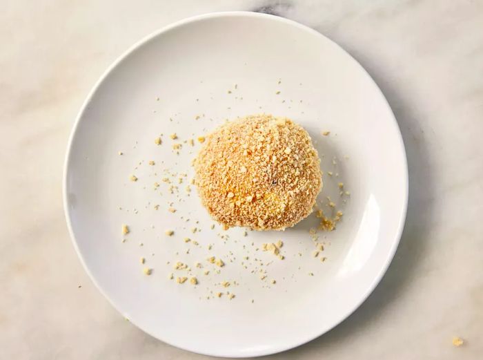 A breaded chicken ball, filled with herb butter, resting on a plate