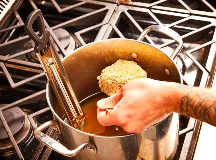 A breaded chicken Kiev being carefully lowered into a pot of hot oil