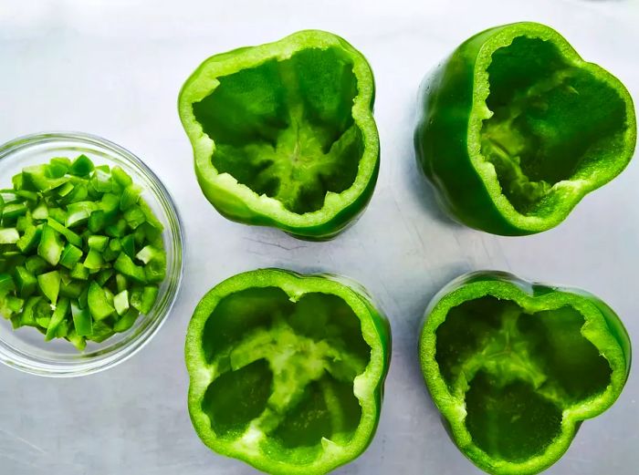 A top-down view of hollowed green peppers with chopped pepper pieces on the side