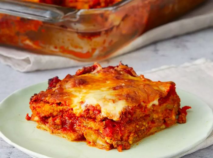 A close-up shot of a single slice of eggplant lasagna with the rest remaining in the casserole dish behind it.