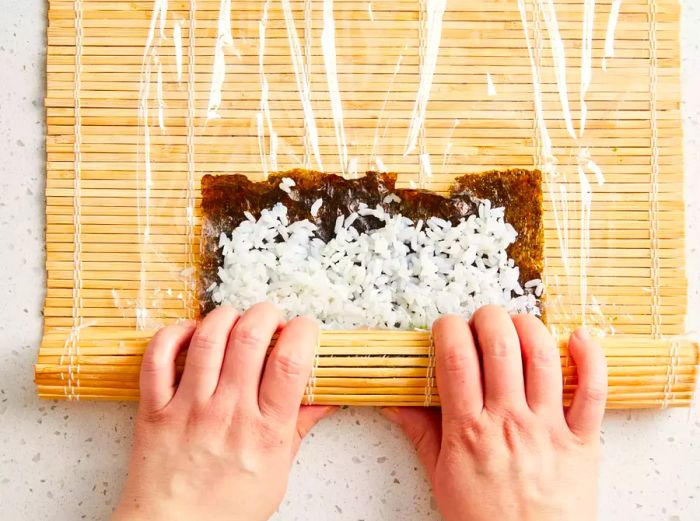 An overhead view of hands rolling sushi into a tight, circular shape