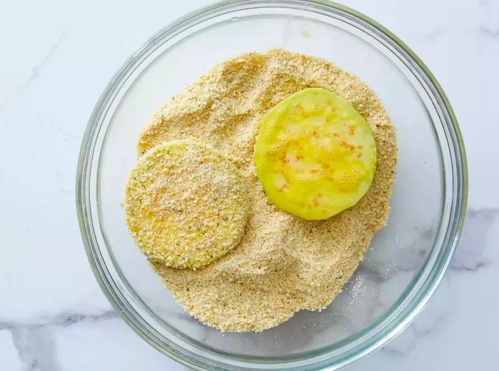 Eggplant slices being coated in breadcrumbs