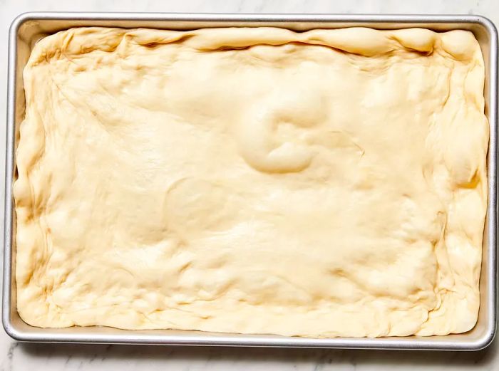 The pizza dough is puffed and stretched to the edges of the baking sheet.