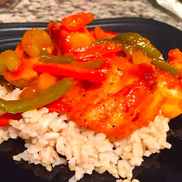 Close-up shot of Sweet and Sour Chicken with peppers served over rice on a black plate