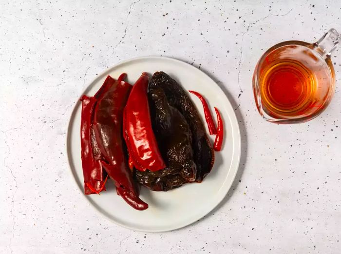 A bowl of rehydrated dried chili peppers, accompanied by a glass measuring cup of the reserved cooking liquid