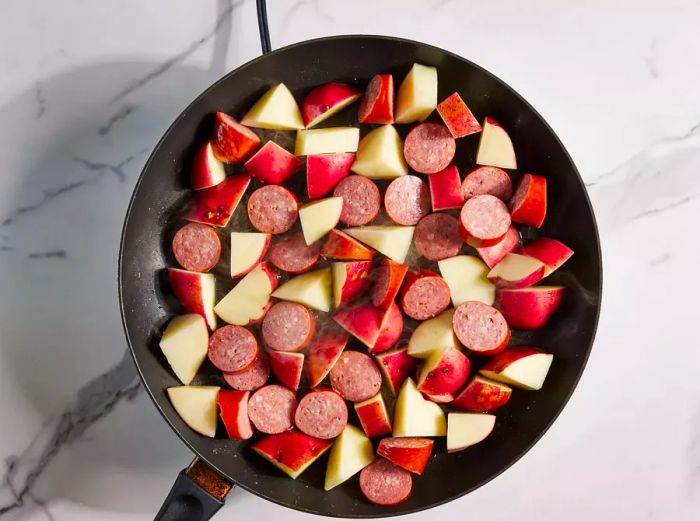 Kielbasa and potatoes cooking in a skillet.