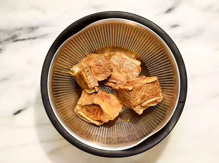 A colander holding the boiled beef short ribs