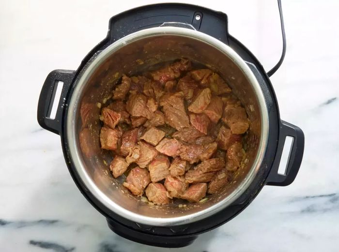 An Instant Pot with browned beef chunks