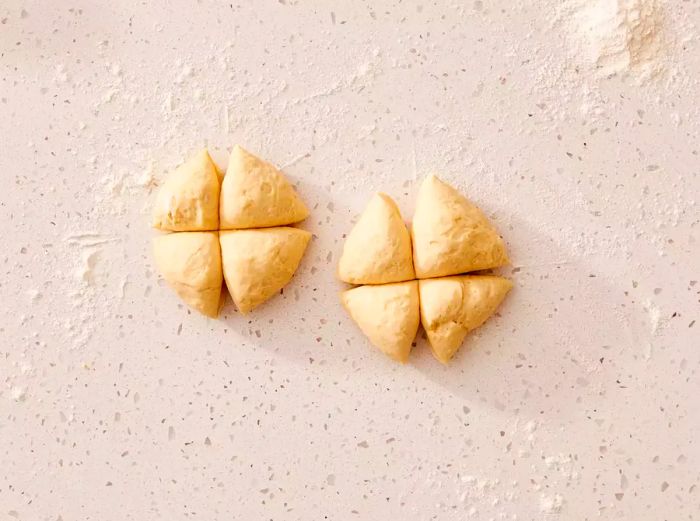 Two dough balls, each divided into four sections on a floured surface