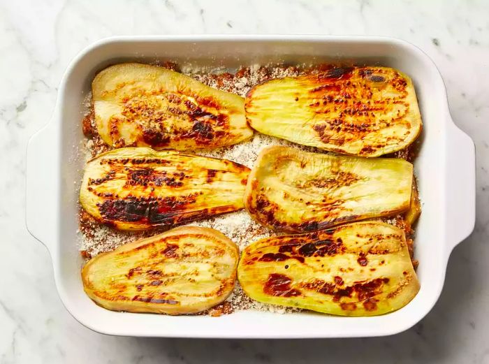 Top view of eggplant slices layered over meat sauce and cheese in a baking dish.