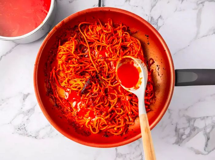 A person pouring tomato broth into a pan with spaghetti.