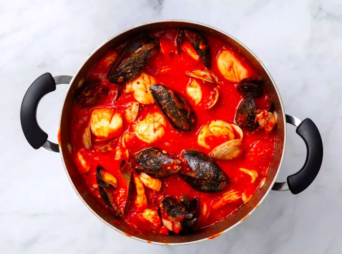 A large pot filled with mussels, clams, calamari, scallops, and shrimp in a rich tomato sauce