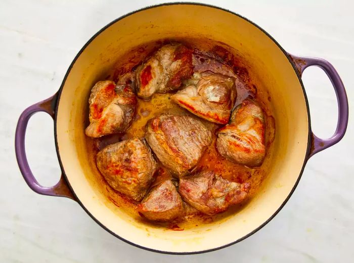 Pork shoulder pieces placed in a Dutch oven with vegetable oil, cooking until they are browned evenly on all sides.