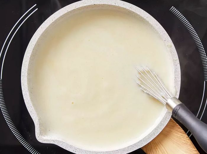 Top view of the milk and butter mixture being whisked and cooked in a saucepan.