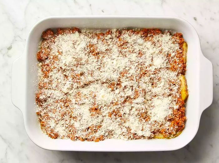 Top view of eggplant slices in a baking dish, topped with meat sauce and Parmesan cheese.