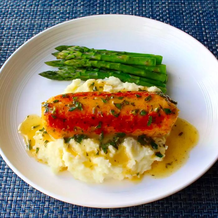 Close-up shot of a Seafood Sausage atop creamy mashed potatoes, accompanied by fresh asparagus on a white plate