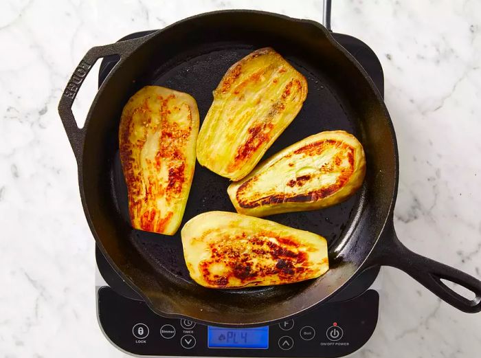 Top view of eggplant slices sizzling in a skillet.