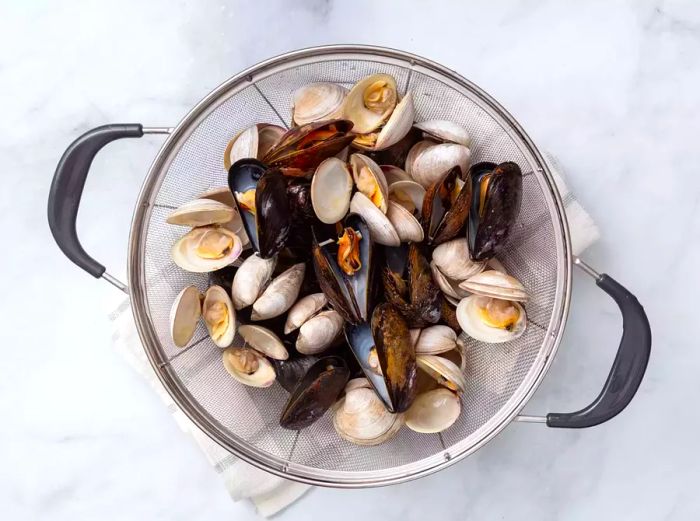 A colander filled with rinsed mussels and opened littleneck clams