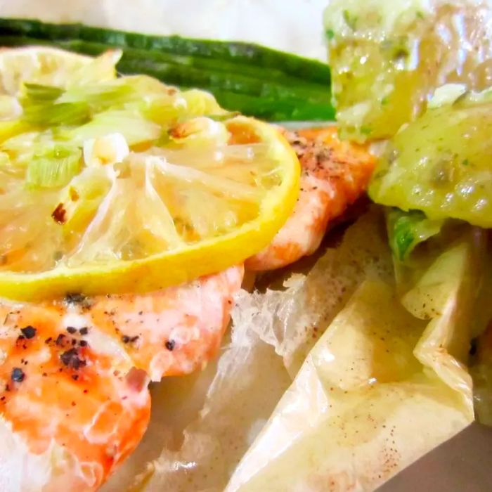 Close-up shot of a salmon fillet en papillote with lemon and herbs, served alongside green beans.