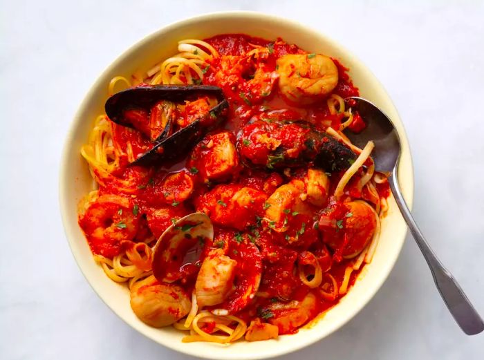 A bowl of zuppa di pesce fra di avolo served over a bed of linguine pasta