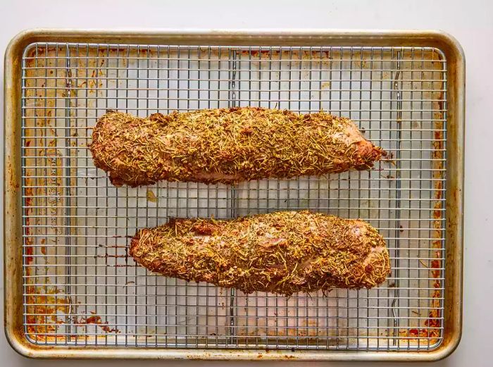 Two perfectly baked Tuscan pork tenderloins resting on a wire rack atop a baking sheet