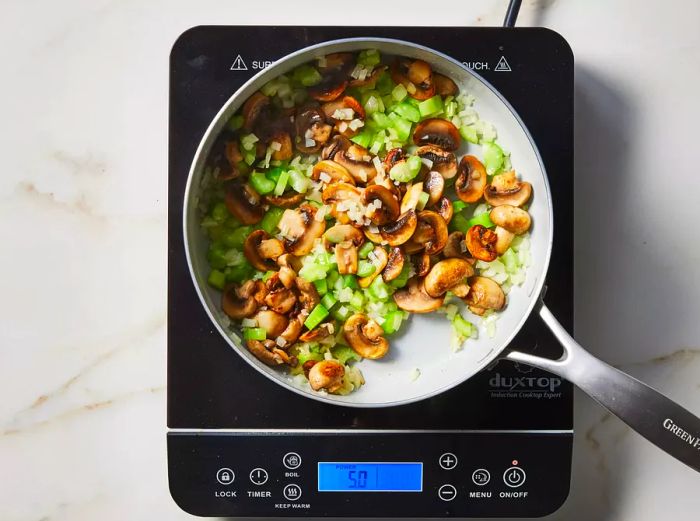 Mushrooms, onions, and celery sautéing in a skillet