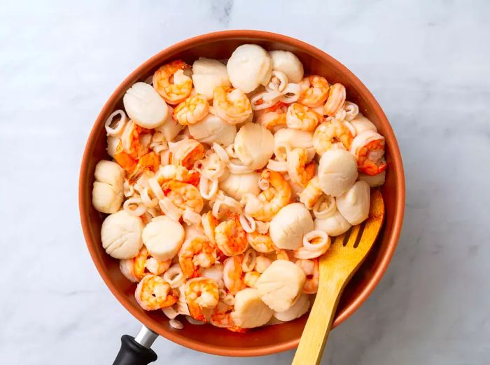 A large skillet with scallops, shrimp, and calamari rings cooking together