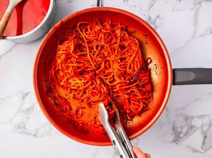 A person tossing spaghetti in a rich tomato sauce.