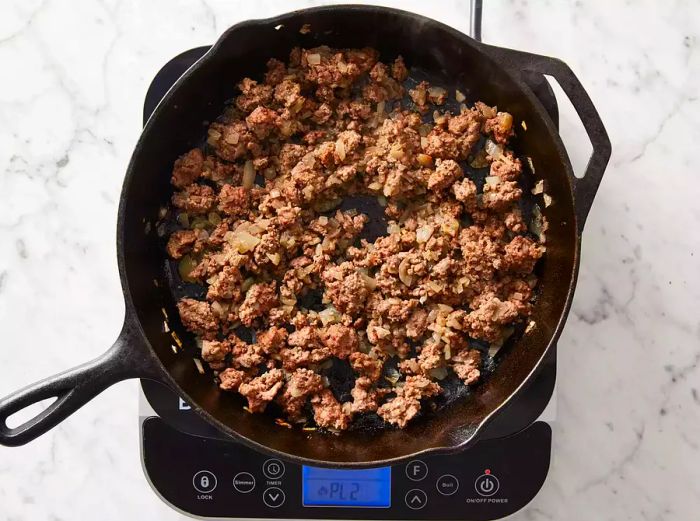 Top view of ground beef, onions, and garlic sizzling in a skillet.