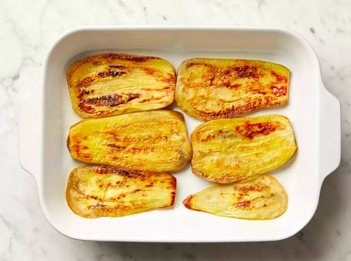 Top view of cooked eggplant slices arranged in a baking dish.