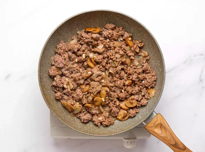 Ground beef and sliced mushrooms frying in a skillet.